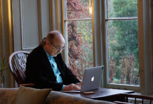 Older man sitting near window viewing online courses for seniors.